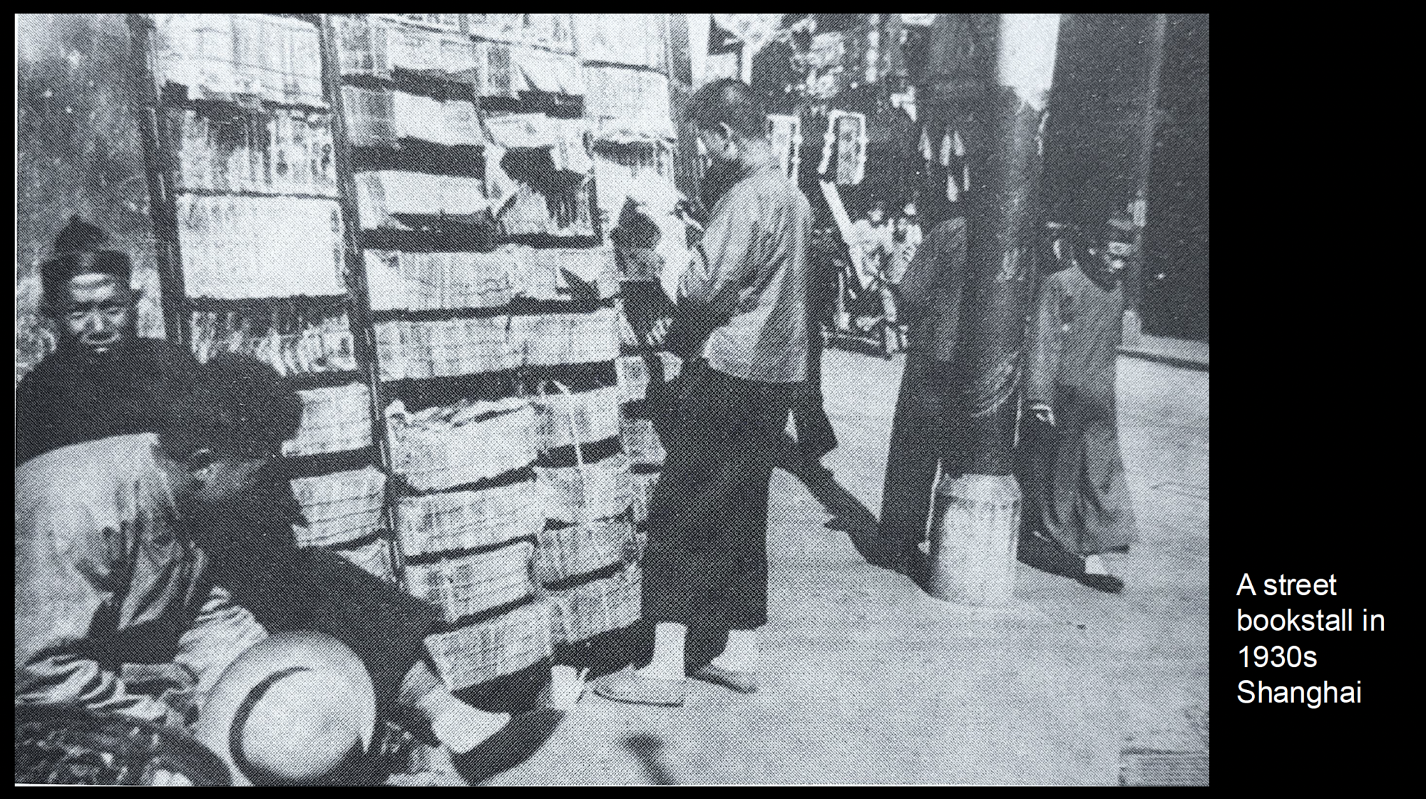 Vintage black-and-white photo of a street bookstall in 1930s Shanghai, China; men browsing magazines and newspapers.