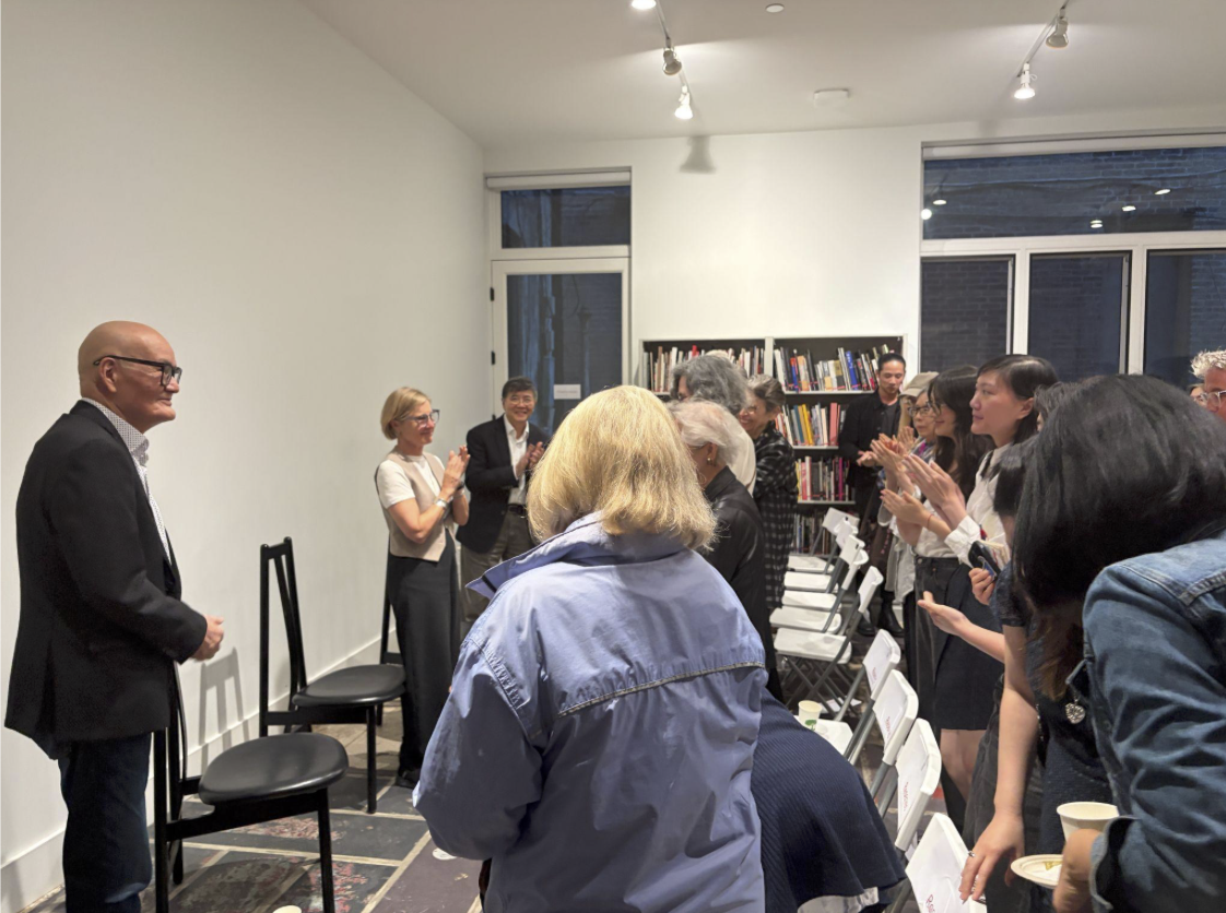 Audience gives standing ovation at author talk in a book-lined event space; speaker at front with chairs in modern room.