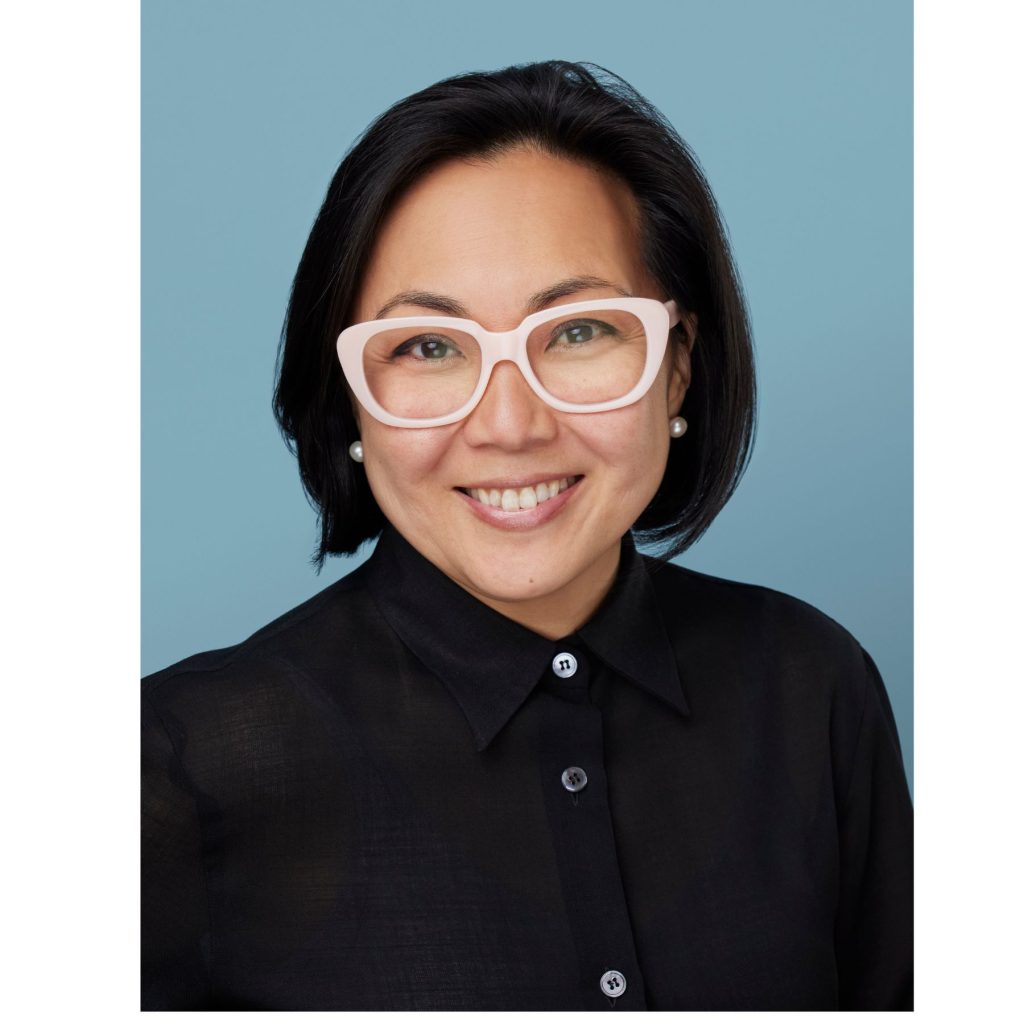 Business headshot of a smiling woman wearing pink glasses and a black shirt on a blue background