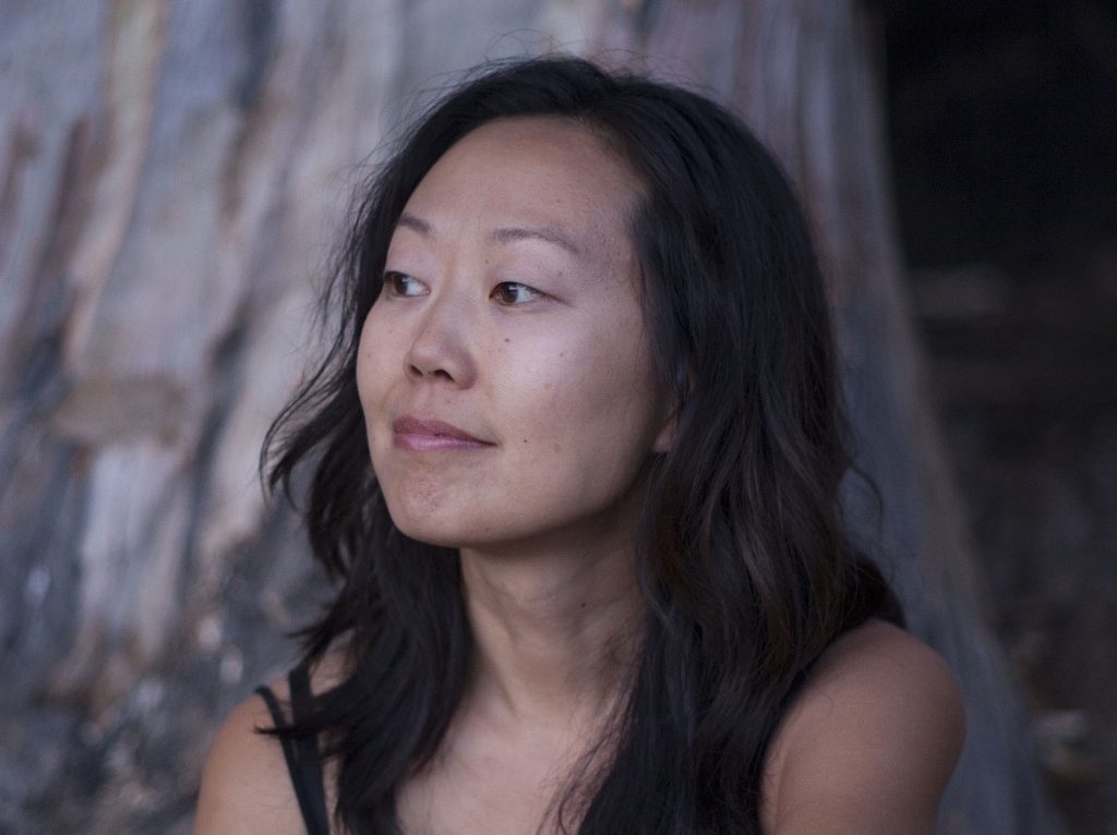 Portrait of a thoughtful woman with long dark hair outdoors, looking left against tree bark background