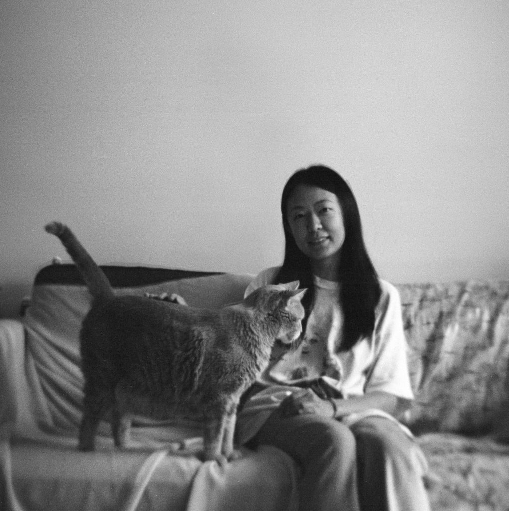 Black-and-white home portrait of a woman on a sofa petting a cat in the living room.