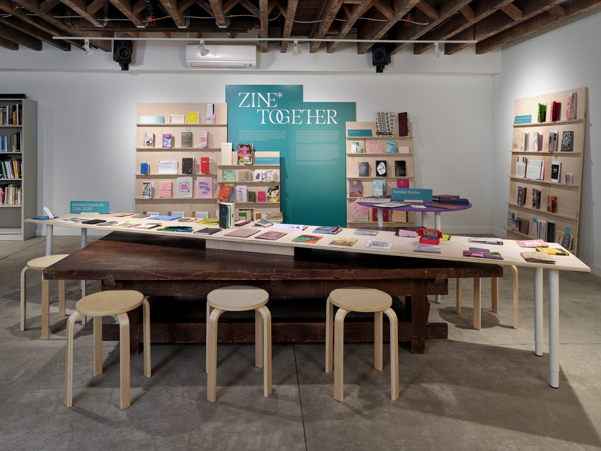 Zine Together exhibition in gallery: colorful indie zines on tables and shelves in creative workshop space