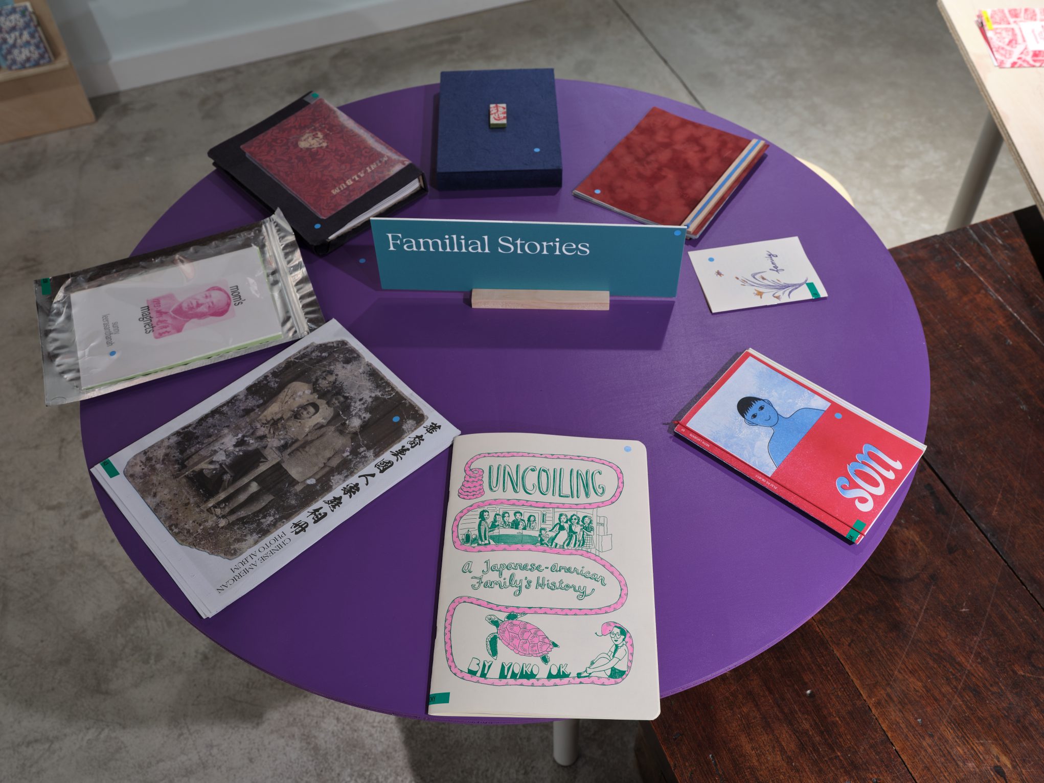 Round purple table display of indie zines and books—'Familial Stories' theme at art bookstore.