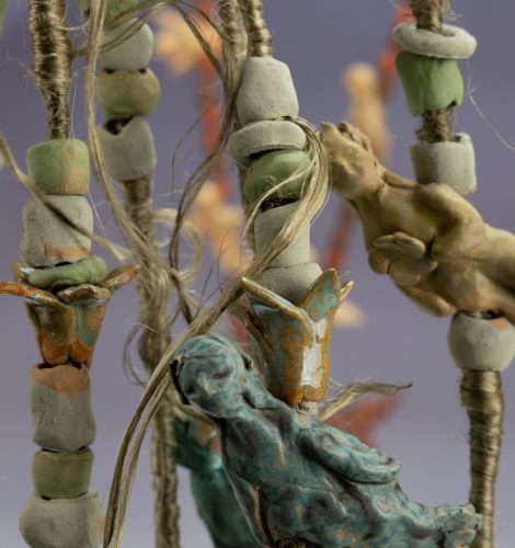 Close-up of handmade ceramic beads and figurine charms strung on twine, rustic glazed pottery art.