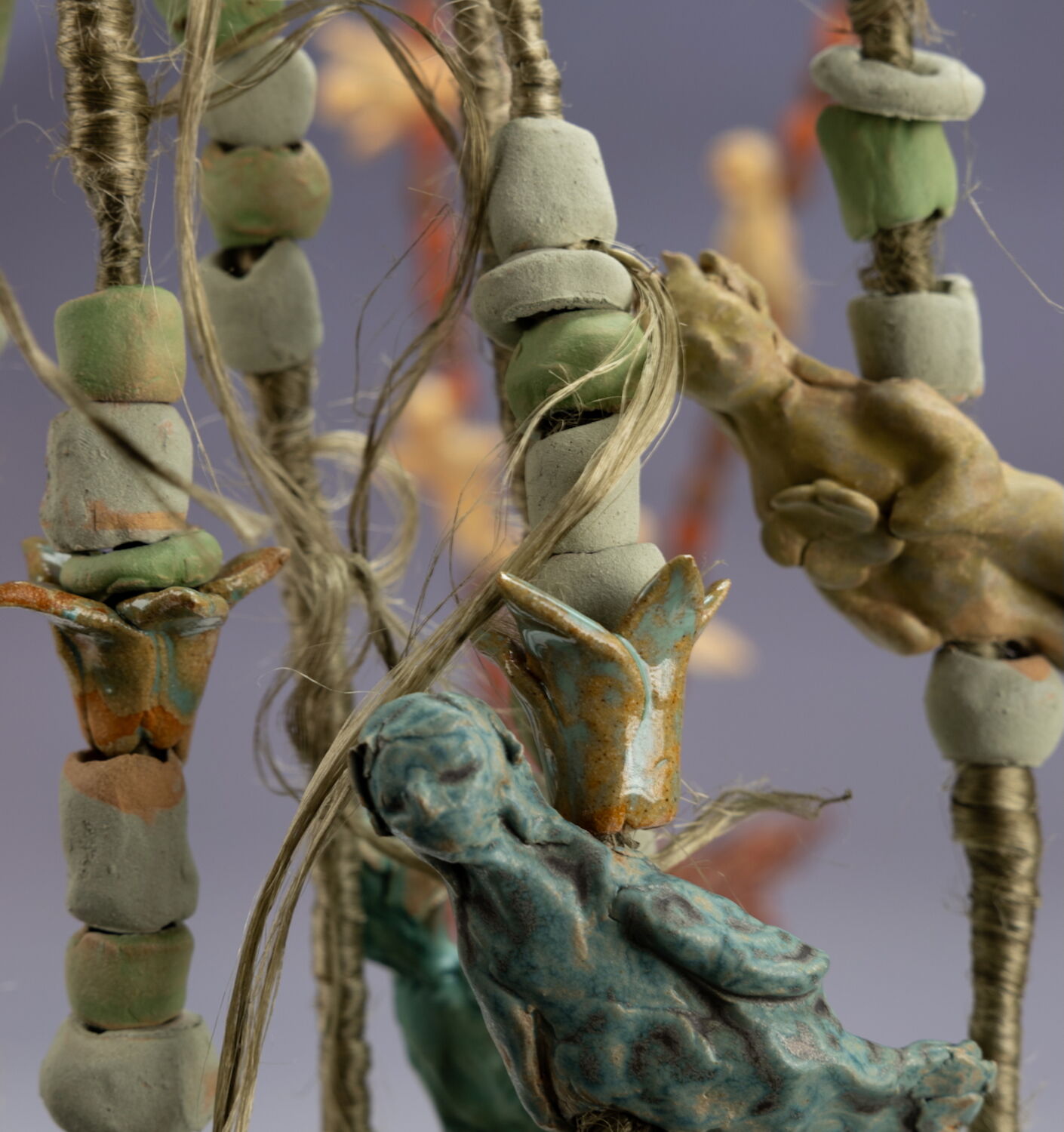 Close-up of handmade ceramic beads and figurine charms strung on twine, rustic glazed pottery art.