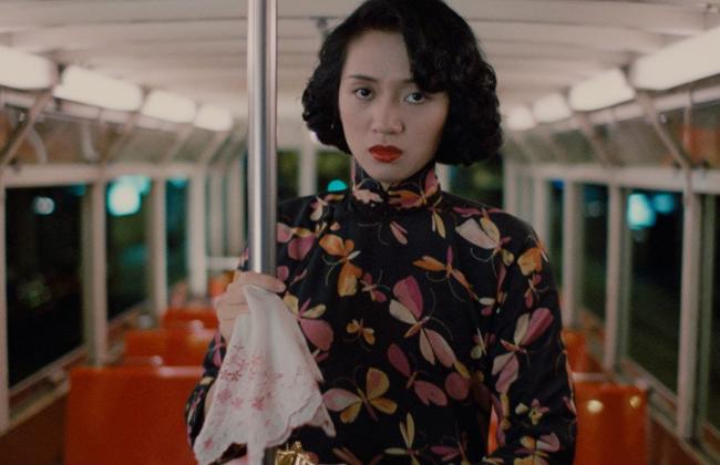 Woman in floral cheongsam on night tram, red lipstick, holding pole and lace handkerchief, moody cinematic scene.