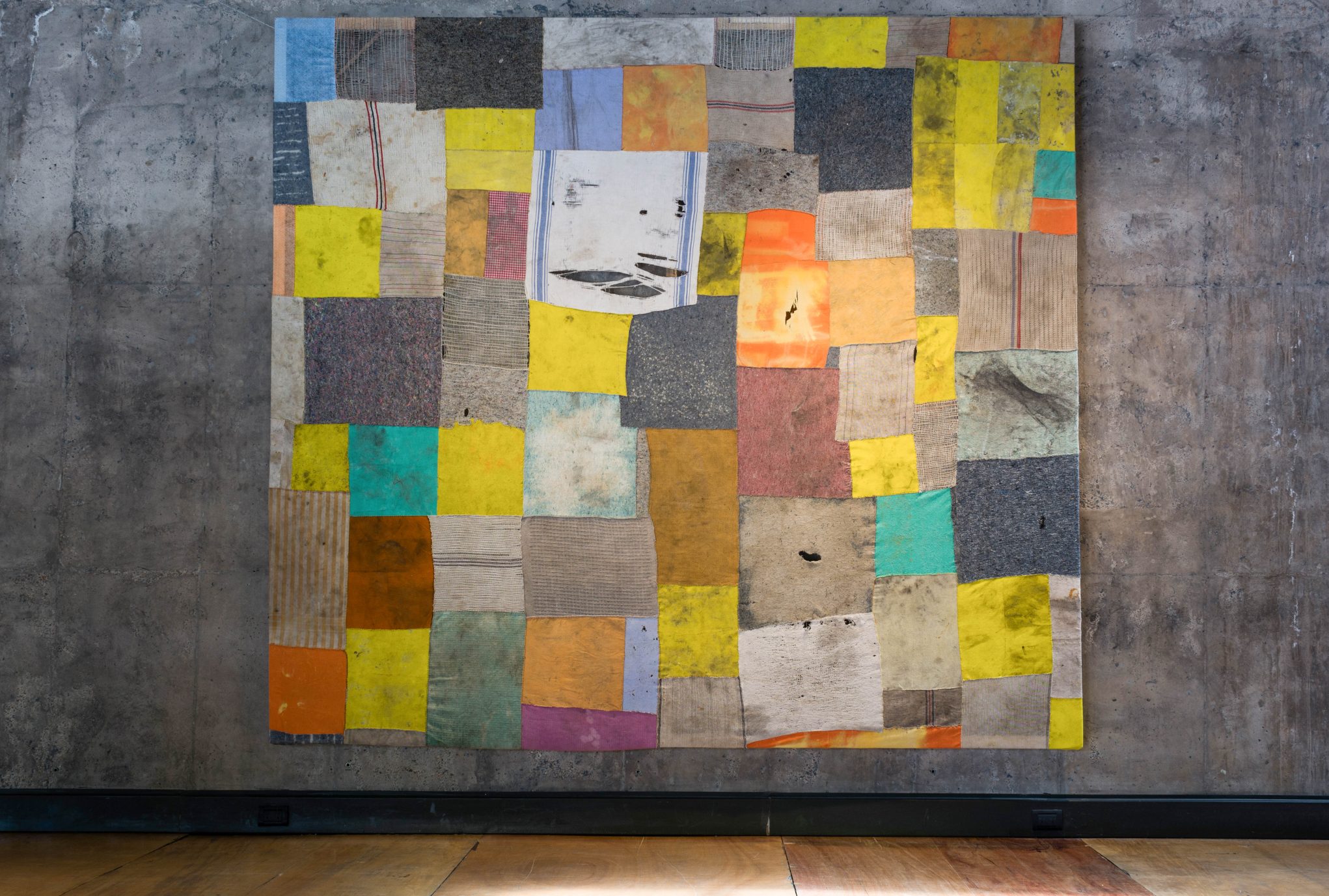 Colorful abstract patchwork collage on concrete wall in modern gallery, mixed-media squares and rectangles artwork