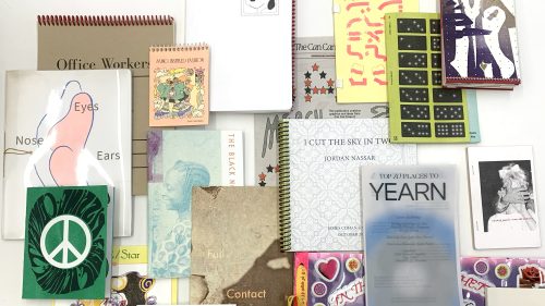 Flat lay of colorful indie zines, spiral notebooks, and art books arranged on a white background.
