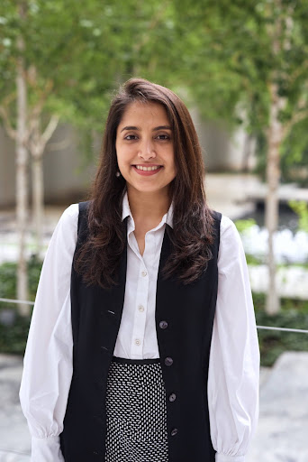 Smiling businesswoman in white blouse and black vest standing in a leafy office courtyard